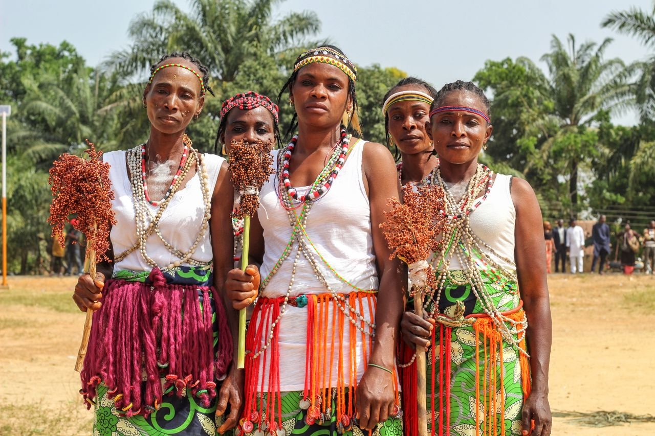 Group of women in traditional attire under palm trees outdoors.